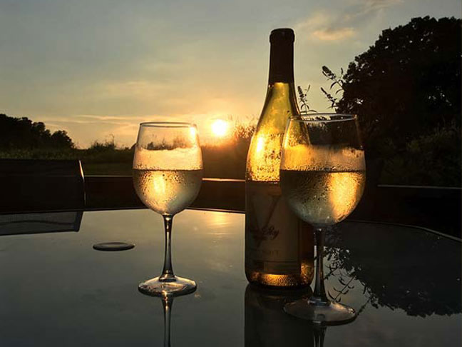 Bottle of Blue Sky Vineyard white wine with two full glasses at sunset