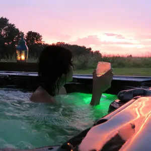 Woman in hot tub holding a glass of wine looking out at sunset on the Shawnee Hills Wine Trail