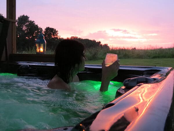 Woman in hot tub holding a glass of wine looking out at sunset on the Shawnee Hills Wine Trail