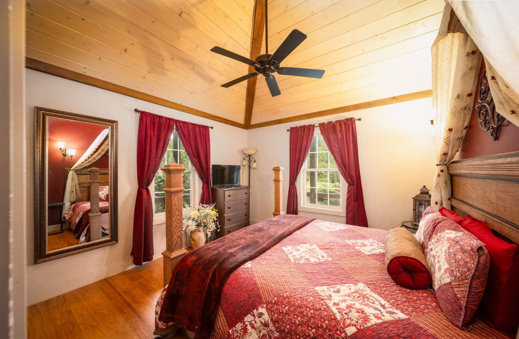 Bedroom with vaulted ceilings, fan, king size hand crafted four post bed, red and cream decor.