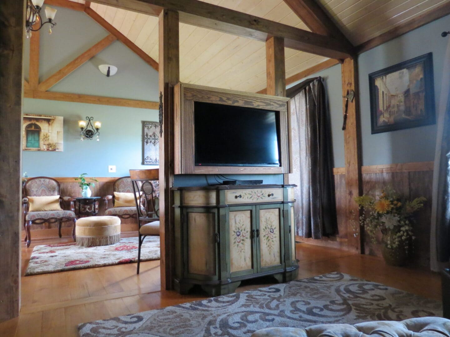 French Cabin parlour with cozy seating area, exposed timber framing, and television concealed within a decorative cabinet.